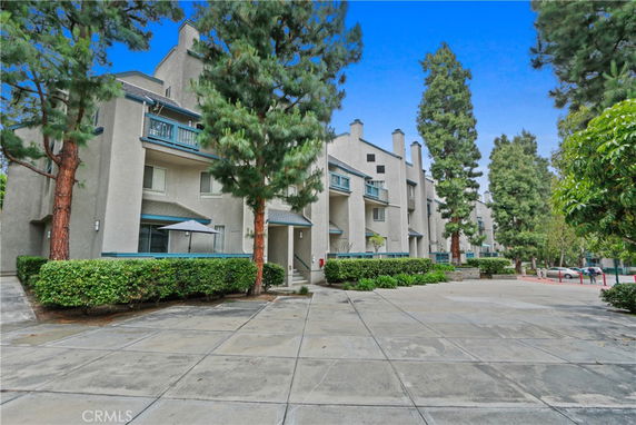 Front view of a multi-story apartment building with balconies and surrounding trees.