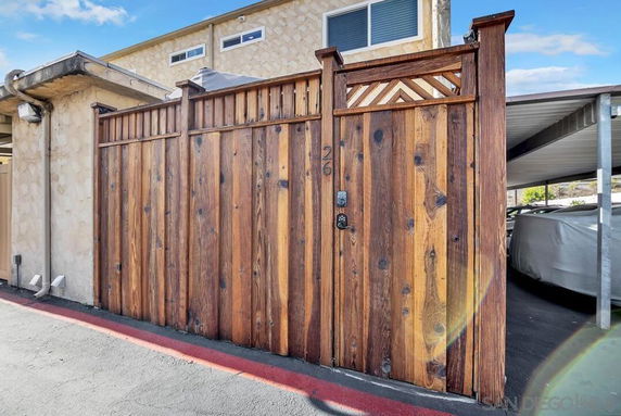 Wooden gate entrance to a covered parking area beside a building.