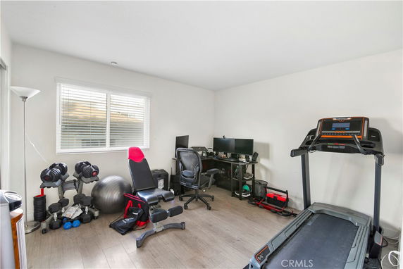 Room with exercise equipment including a treadmill, bench, and dumbbells.