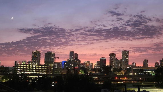 Panoramic view of a city skyline at sunset with a crescent moon.