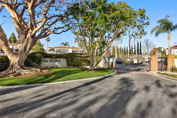 Entrance to a gated residential community with a sign reading 'Villa Pacifica' and trees surrounding the entrance.