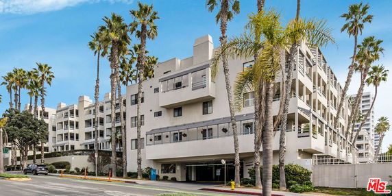 Front view of a multi-story apartment building with balconies and palm trees.