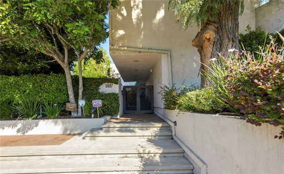 Entrance of a building with steps leading up, surrounded by greenery.