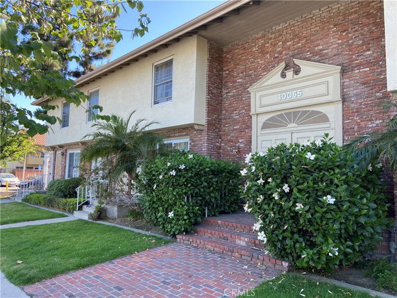 Front view of a two-story house with brick and stucco exterior and stairs leading to the entrance.