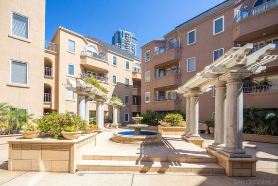 Front view of a multi-story residential building with balconies and a courtyard featuring a fountain and decorative columns.