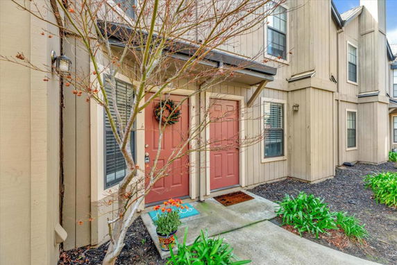Front view of a townhouse with beige siding and red doors.
