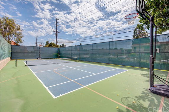 Outdoor tennis and basketball court surrounded by a fence.