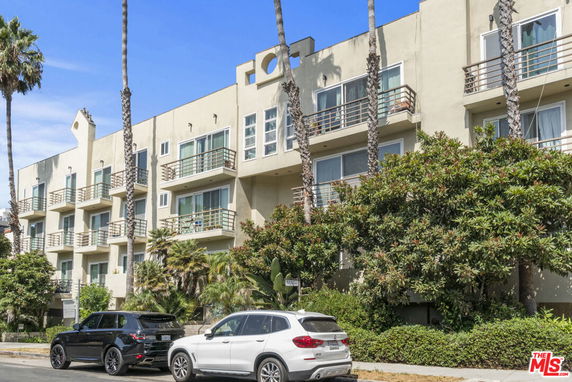 Front view of a multi-story building with balconies and palm trees.
