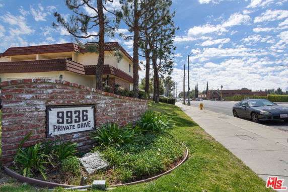 Front view of a two-story house with a brick fence and a private drive sign.