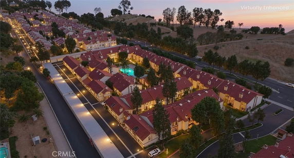 Aerial view of a residential complex with multiple buildings and a central swimming pool, set in a hilly landscape.