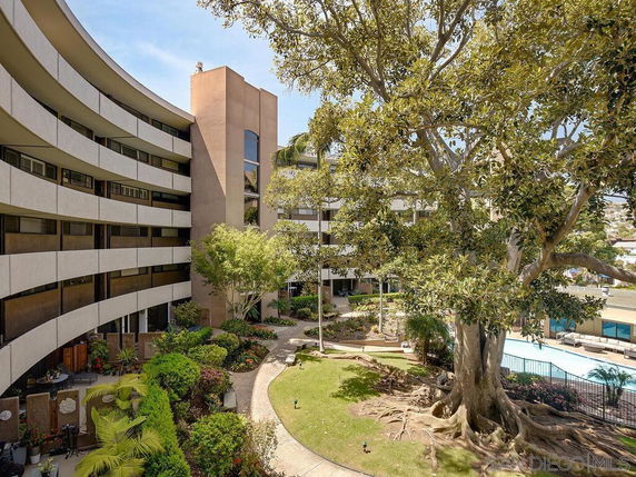 Multi-story building with a curved facade and a large tree in the courtyard.