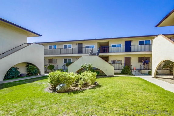 View of a two-story residential building complex with balconies and green lawn.