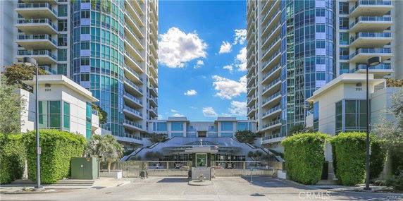Front view of a tall modern apartment complex with two towers and a gated entrance.
