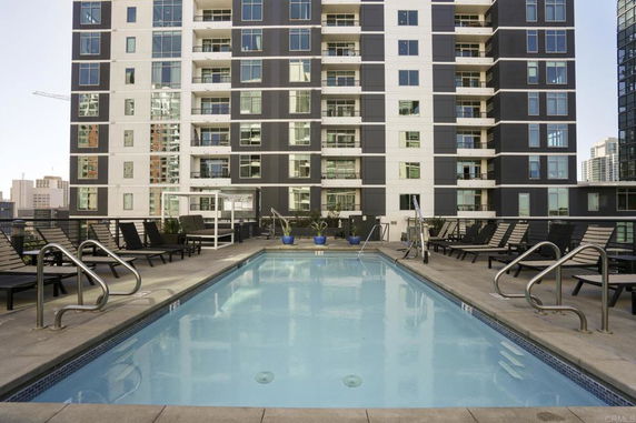 Swimming pool area in front of a tall building with lounge chairs nearby.
