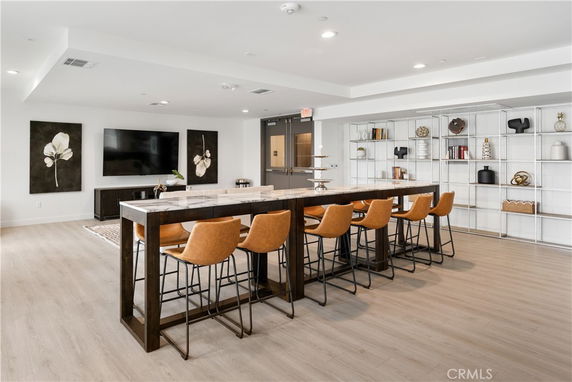 Interior of a modern clubhouse with a long table and chairs, wall-mounted TV, and decorative shelves.