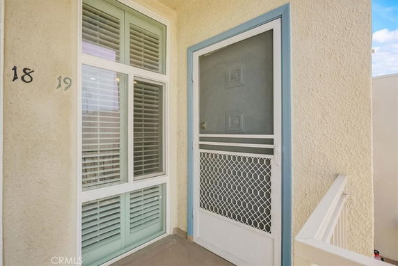 Close-up view of the entrance to a building unit with numbers 18 and 19, featuring a light-colored exterior and a door with a metal mesh screen.