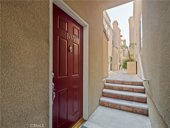 Front view of building entrance with a red door marked 106 and adjacent steps leading to walkway.