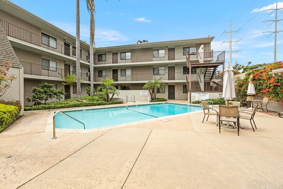 Outdoor swimming pool area in front of a multi-story residential building.
