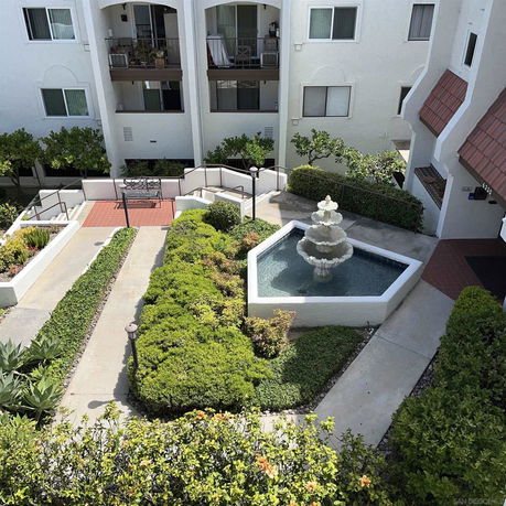 View of an apartment building courtyard with a fountain and landscaped greenery.