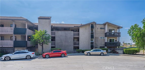 Front view of a multi-story residential building with balconies and parked cars in front.
