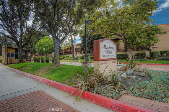Entrance view of MacArthur Village Condominiums with surrounding trees and a sign.