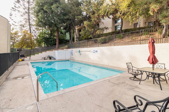 Outdoor swimming pool with patio furniture and surrounding trees.