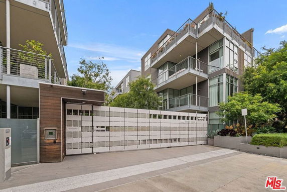 Front view of a modern multi-story building with balconies and a gated entrance.