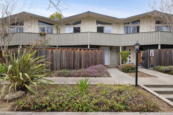 Front view of a two-story house with a wooden fence and plants in the front yard.