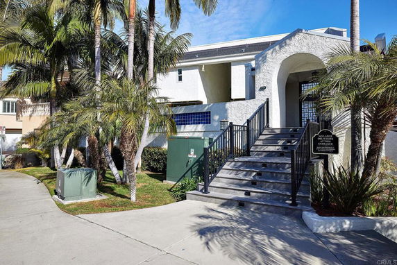 Front view of a house with steps leading to the entrance and tropical plants around.