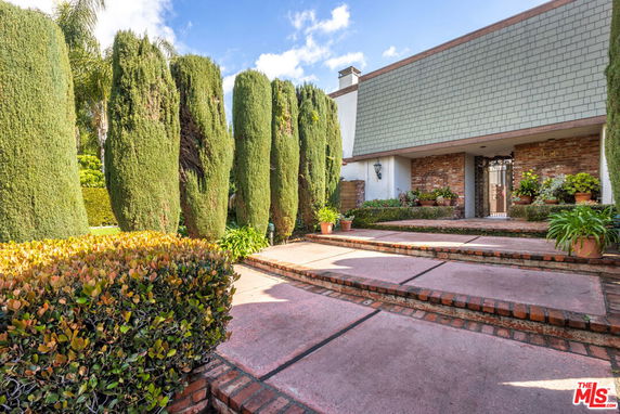 Front view of a house with a brick pathway and tall hedges.