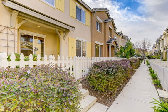 Front view of a row of two-story houses with a white picket fence.