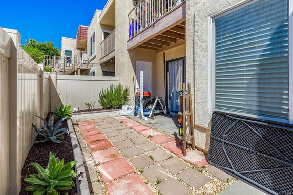 Patio area behind a multi-story building with fenced boundaries and potted plants.
