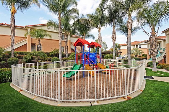Outdoor play area with a playground and surrounding buildings.