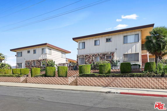 Front view of two adjacent two-story apartment buildings with sloped roofs and landscaped hedges.