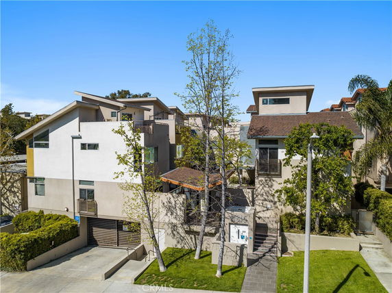 Front view of a multi-story modern house with angular rooflines and trees in front.