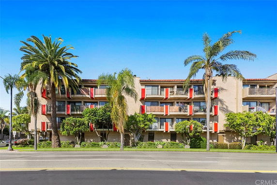 Front view of a multi-story residential building with balconies and surrounding palm trees.