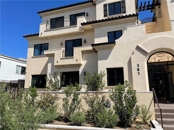 Front view of a multi-story house with balconies and arched entrance.