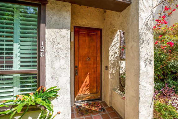 Front entrance of a house with a wooden door and adjacent window with shutters.
