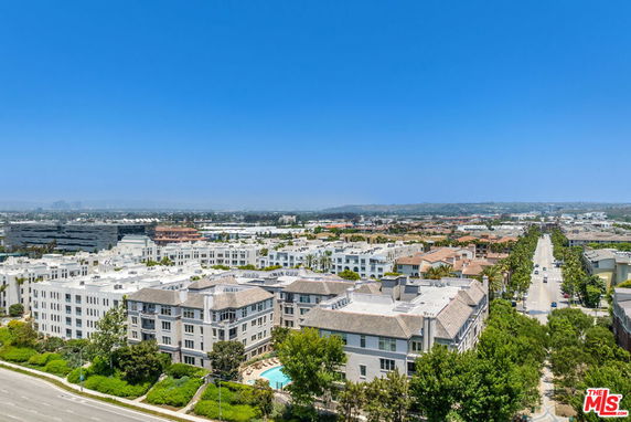 Panoramic view of residential and commercial buildings with roads and trees, seen from above.