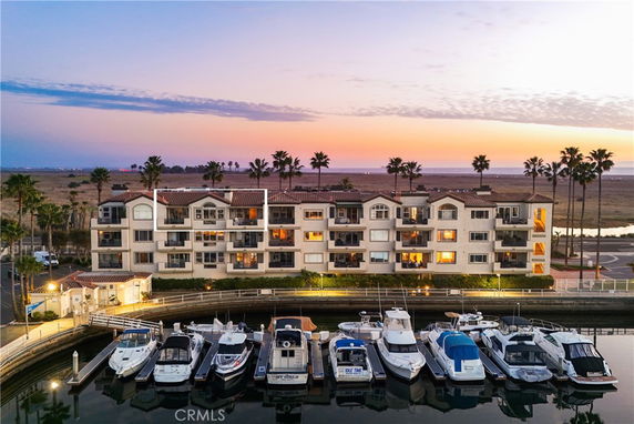 Front view of a multi-story apartment building with balconies, located near a marina.
