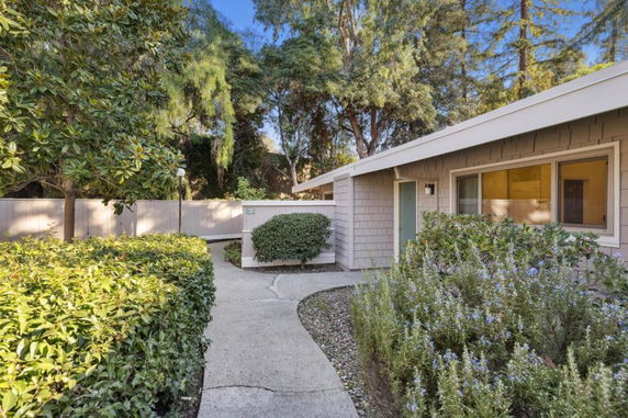 Front view of a single-story house surrounded by bushes and trees.