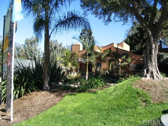 Front view of a house with a stucco exterior and a chimney, surrounded by lush greenery and palm trees.