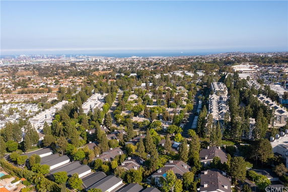 Aerial panoramic view of a residential area with houses and trees, distant cityscape and ocean visible on the horizon.