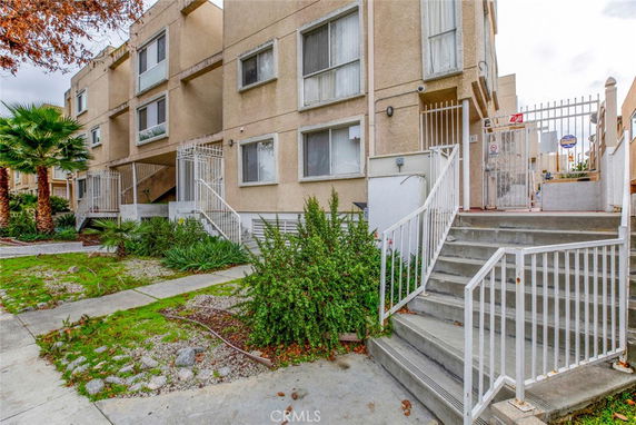 Front view of a multi-story residential building with gated entry and stairs.