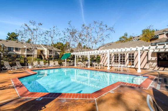 Outdoor swimming pool area with patio chairs and pergola.