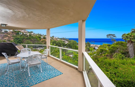 Covered outdoor patio with a table set offering a panoramic view of the ocean and surrounding landscape.