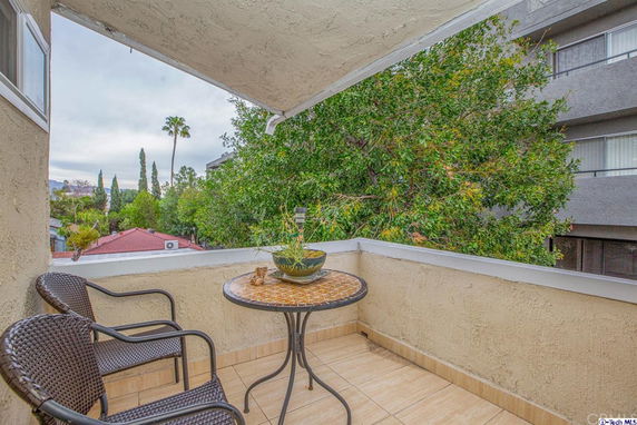 View from a balcony with a small round table and two chairs overlooking trees and neighboring buildings.
