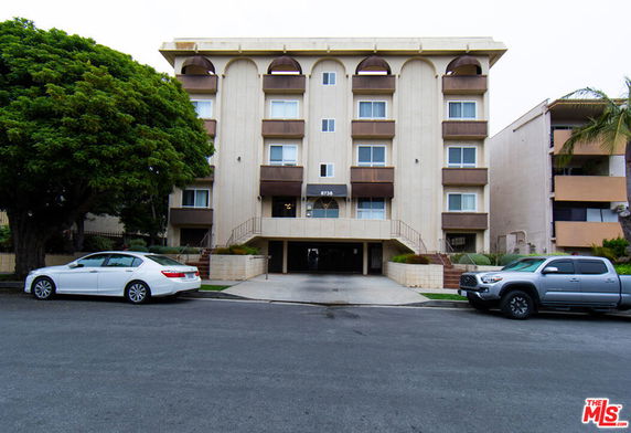 Front view of a multi-story residential building with balconies and surrounding greenery.