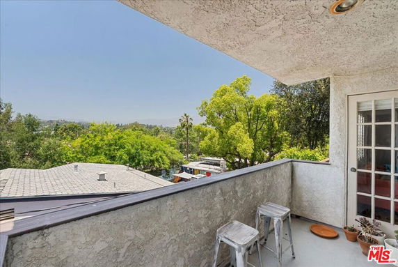 Outdoor balcony with stools overlooking a view of trees and rooftops.