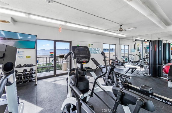 Gym area with exercise equipment and a view of the outside beach through large windows.
